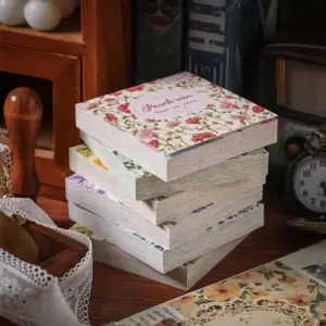 Gestapelte Blöcke mit Blumenmuster-Papier auf einem Holztisch neben Spitze