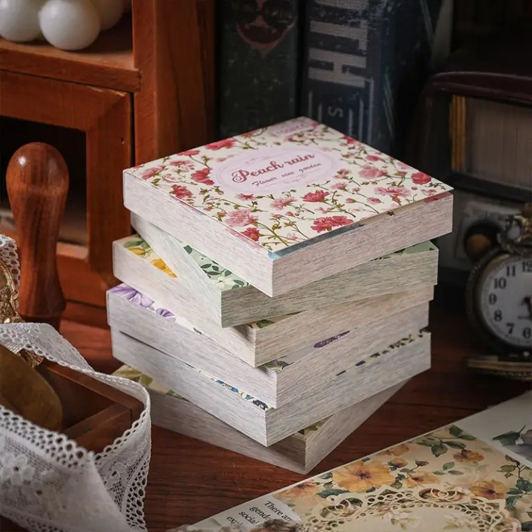Gestapelte Blöcke mit Blumenmuster-Papier auf einem Holztisch neben Spitze