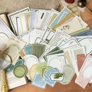 Notizpapiere und Etiketten in Grün, Blau und Beige mit Rahmen und Schriftzügen, auf Holz ausgebreitet