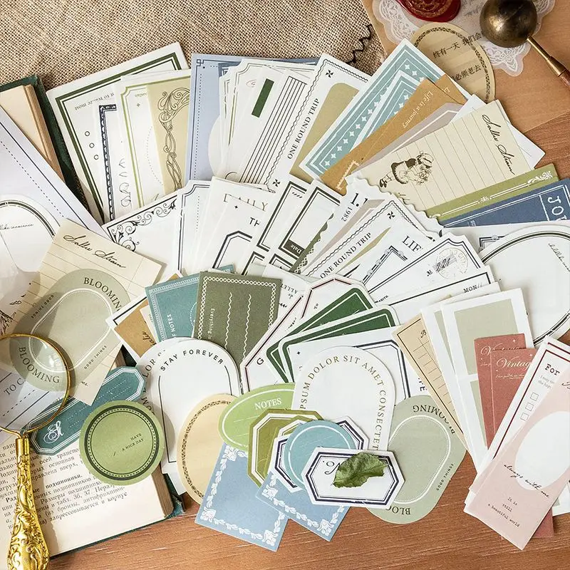 Notizpapiere und Etiketten in Grün, Blau und Beige mit Rahmen und Schriftzügen, auf Holz ausgebreitet