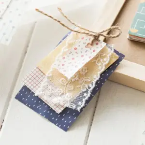 Gemusterte Bastelpapier-Karten mit Spitze und Anhänger auf weißem Holz