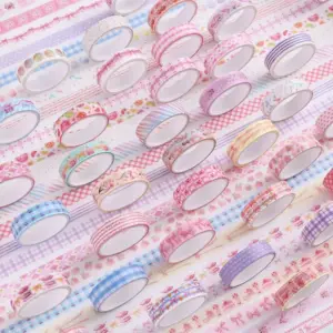 Rosa und blaue Washi-Tape-Rollen mit Mustern, lose verteilt auf gemustertem Hintergrund